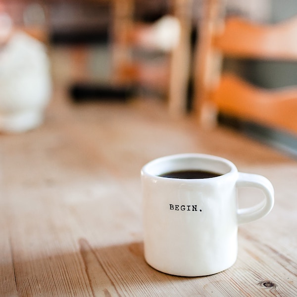 a white mug filled with coffee, stamped with the word BEGIN