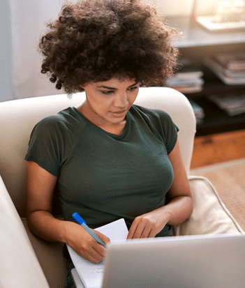 Woman taking notes on notepad while looking at a computer screen